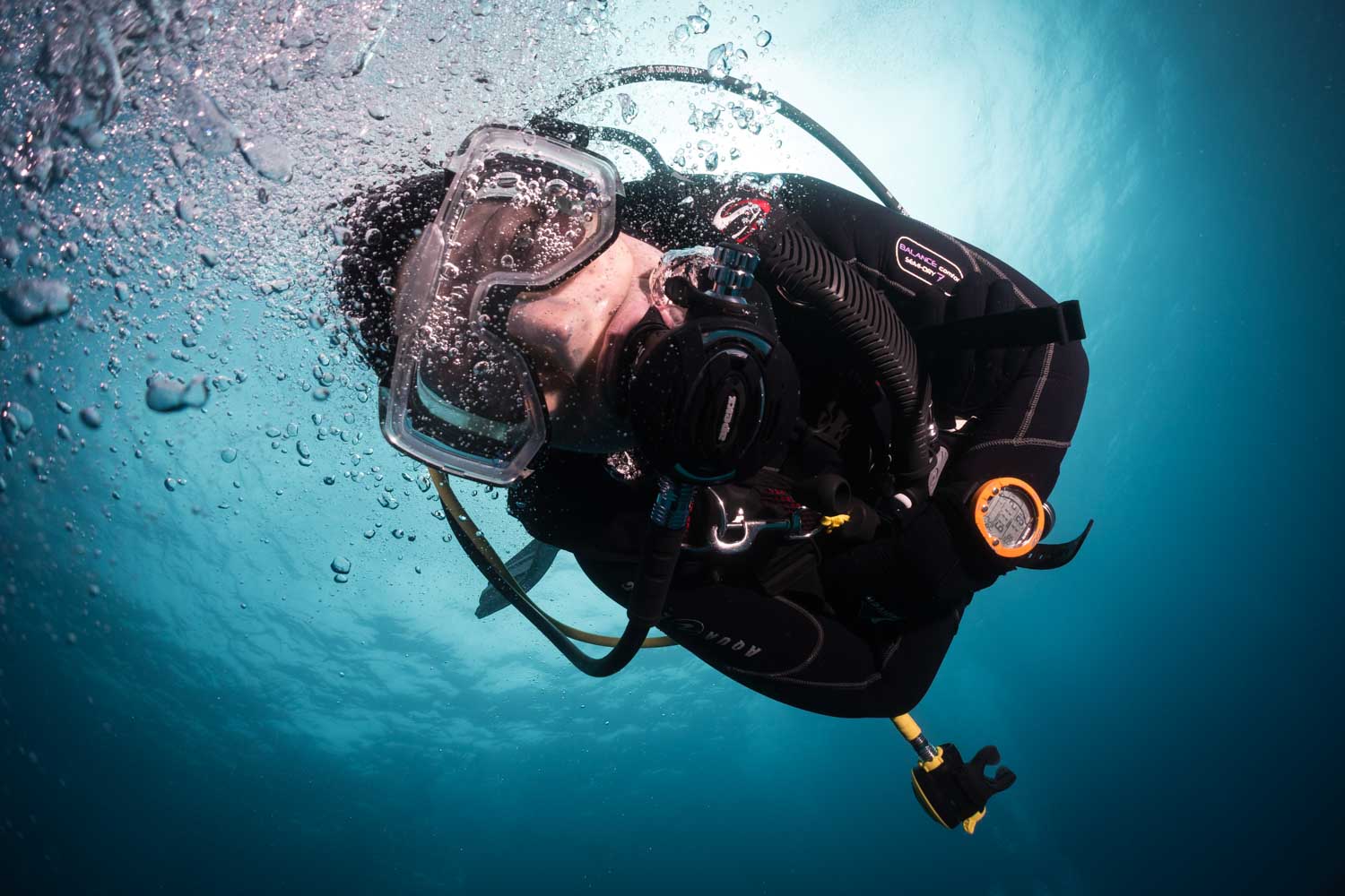 Scuba diver underwater surrounded by bubbles, wearing a mask and suit, exploring the deep blue sea.
