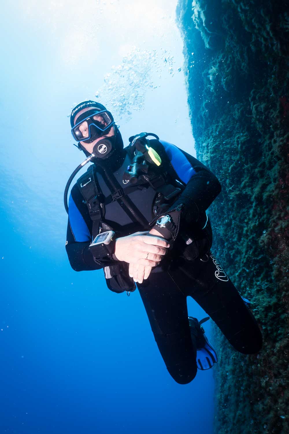 Scuba diver in wetsuit and gear exploring an underwater reef, surrounded by clear blue ocean water.