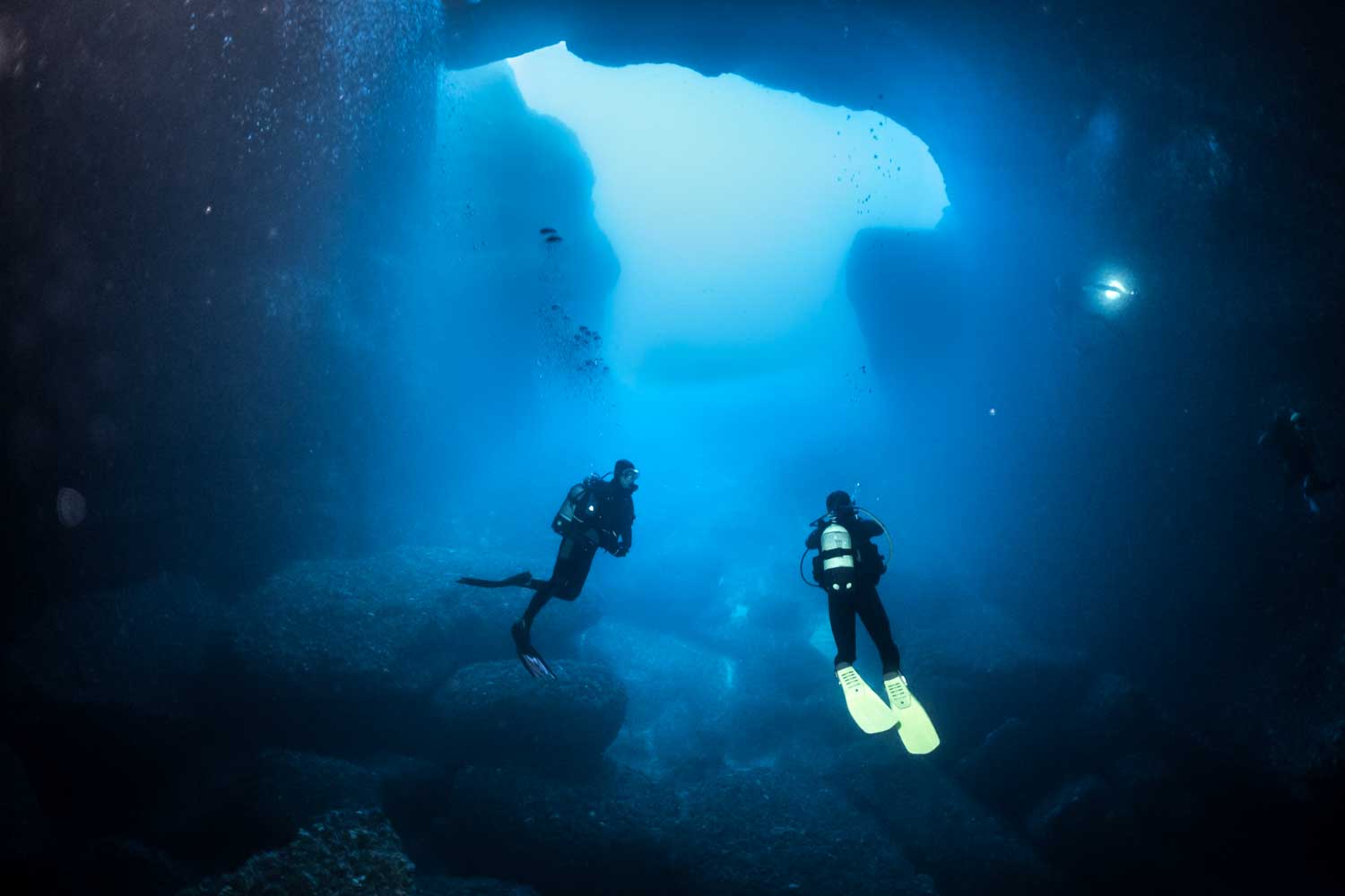 Scuba divers exploring an underwater cave with clear blue water and rocky formations.