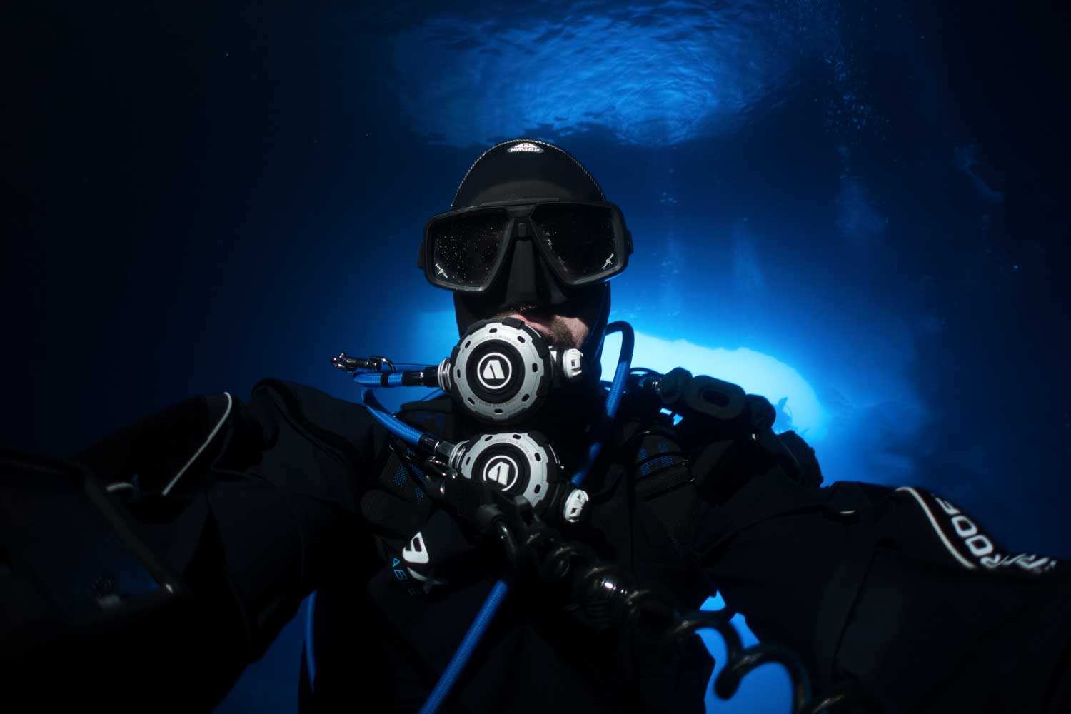 Scuba diver with mask and gear illuminated by deep blue underwater light.