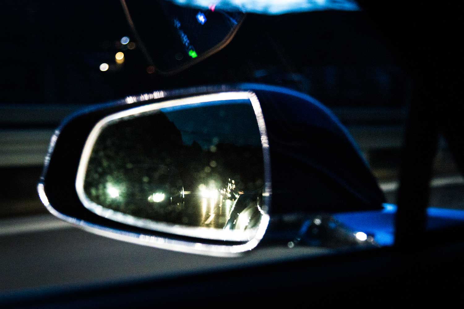 Car side mirror reflecting headlights on a dark road.