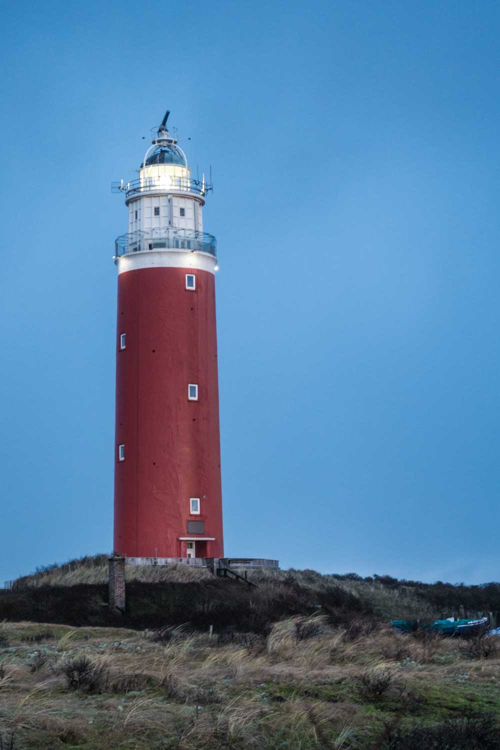 Red lighthouse on a grassy hill against a clear blue sky at dusk.