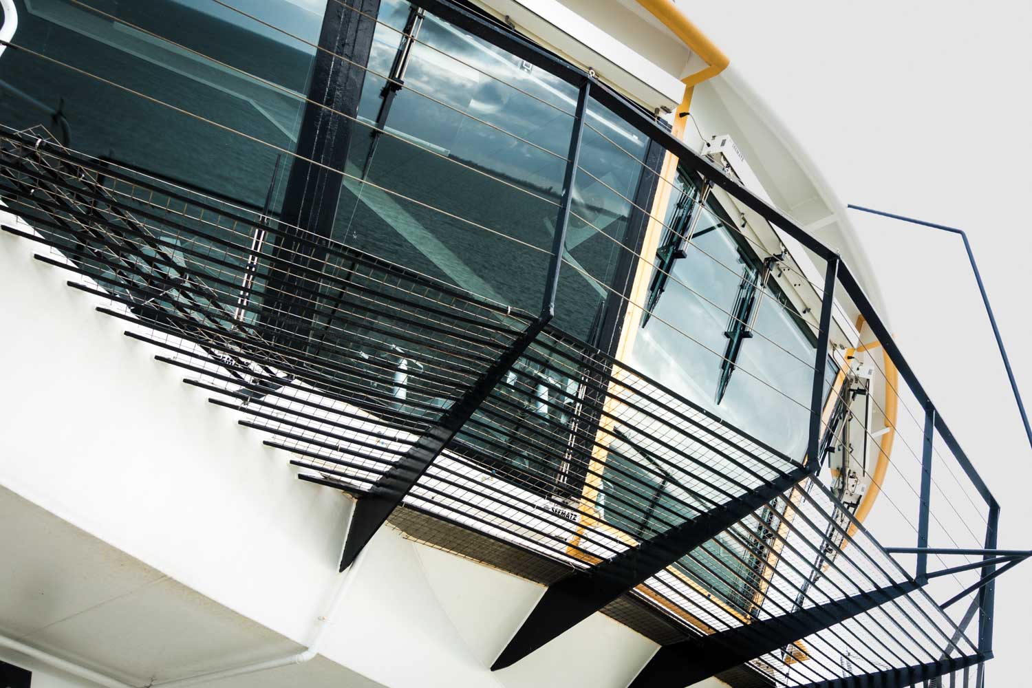 Modern glass-front balcony with sleek black railing overlooking water.