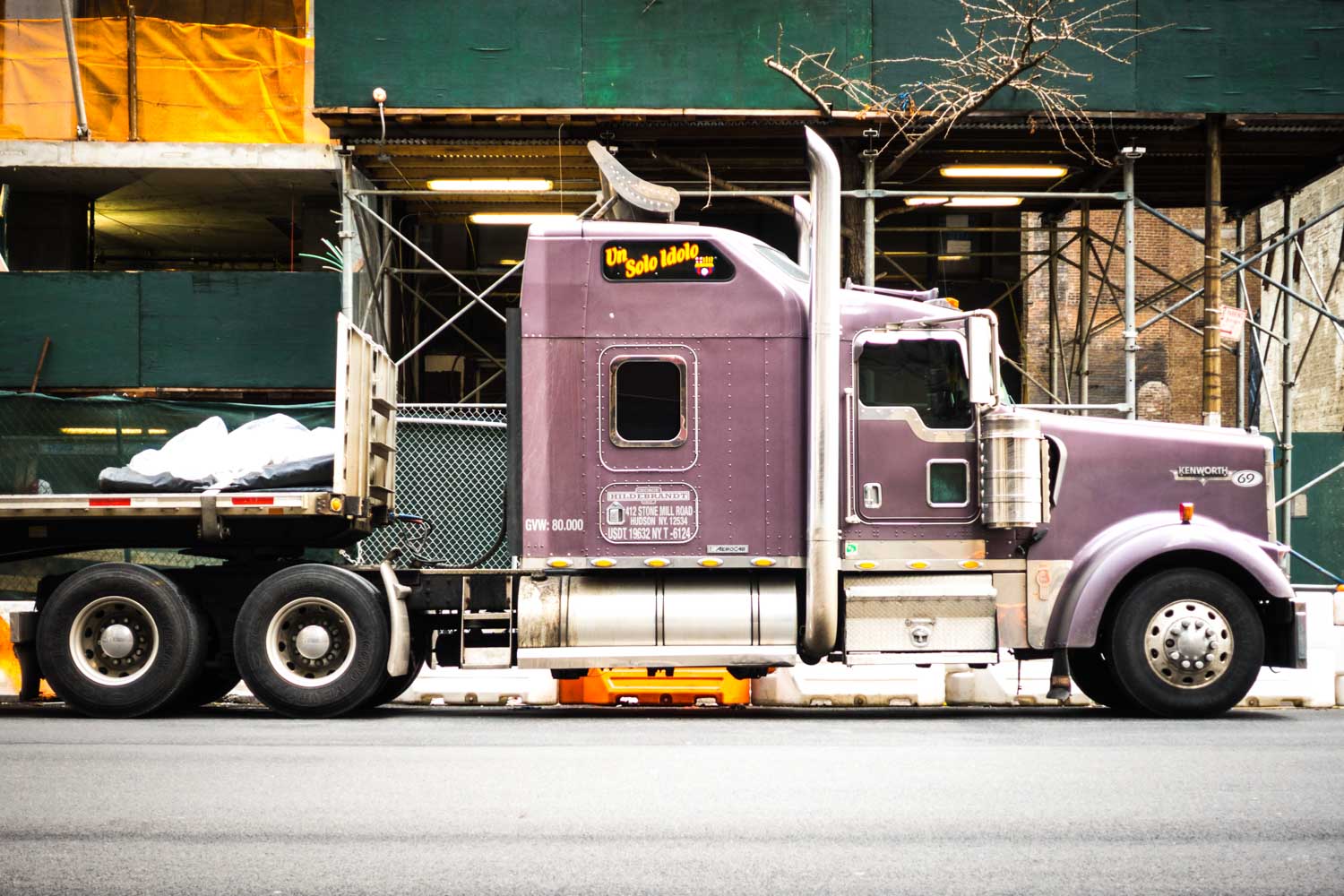 Purple semi-truck parked beside a construction site with scaffolding, displaying Un Solo Idolo on its front.