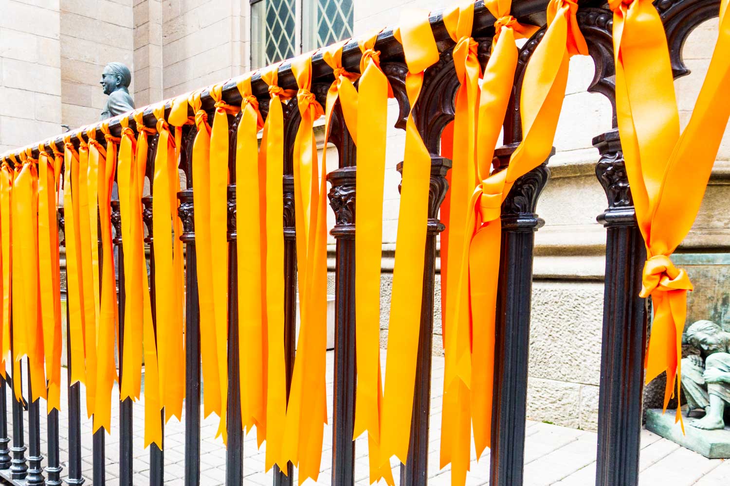 Bright orange ribbons tied to a black iron fence in front of a historic building.