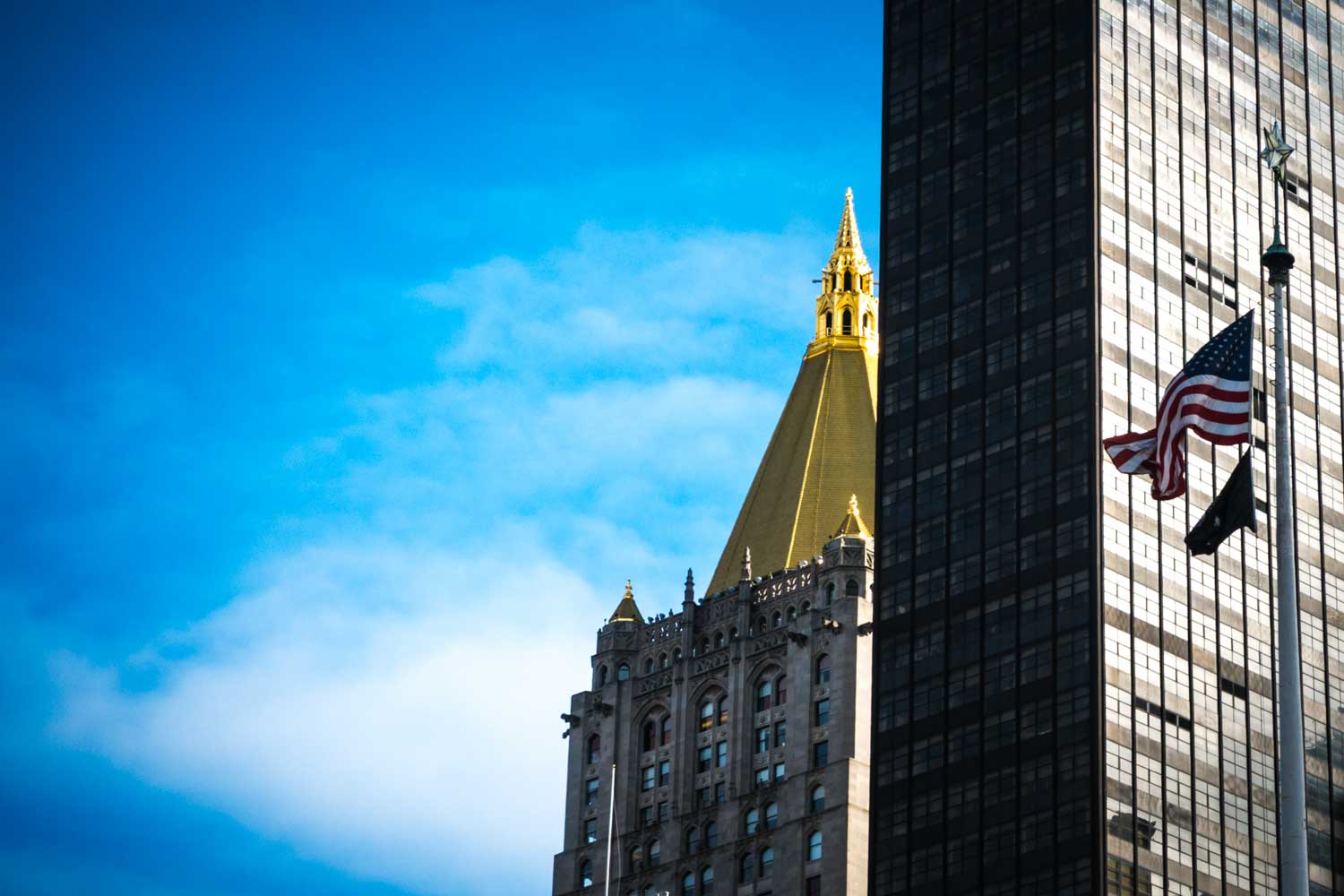 Golden-topped skyscraper with American flag and blue sky backdrop, highlighting urban architecture.