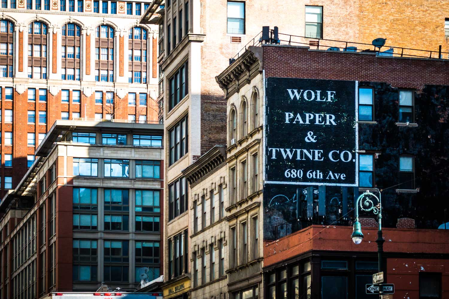 Urban street view with vintage Wolf Paper & Twine Co. sign on a building in a cityscape setting.