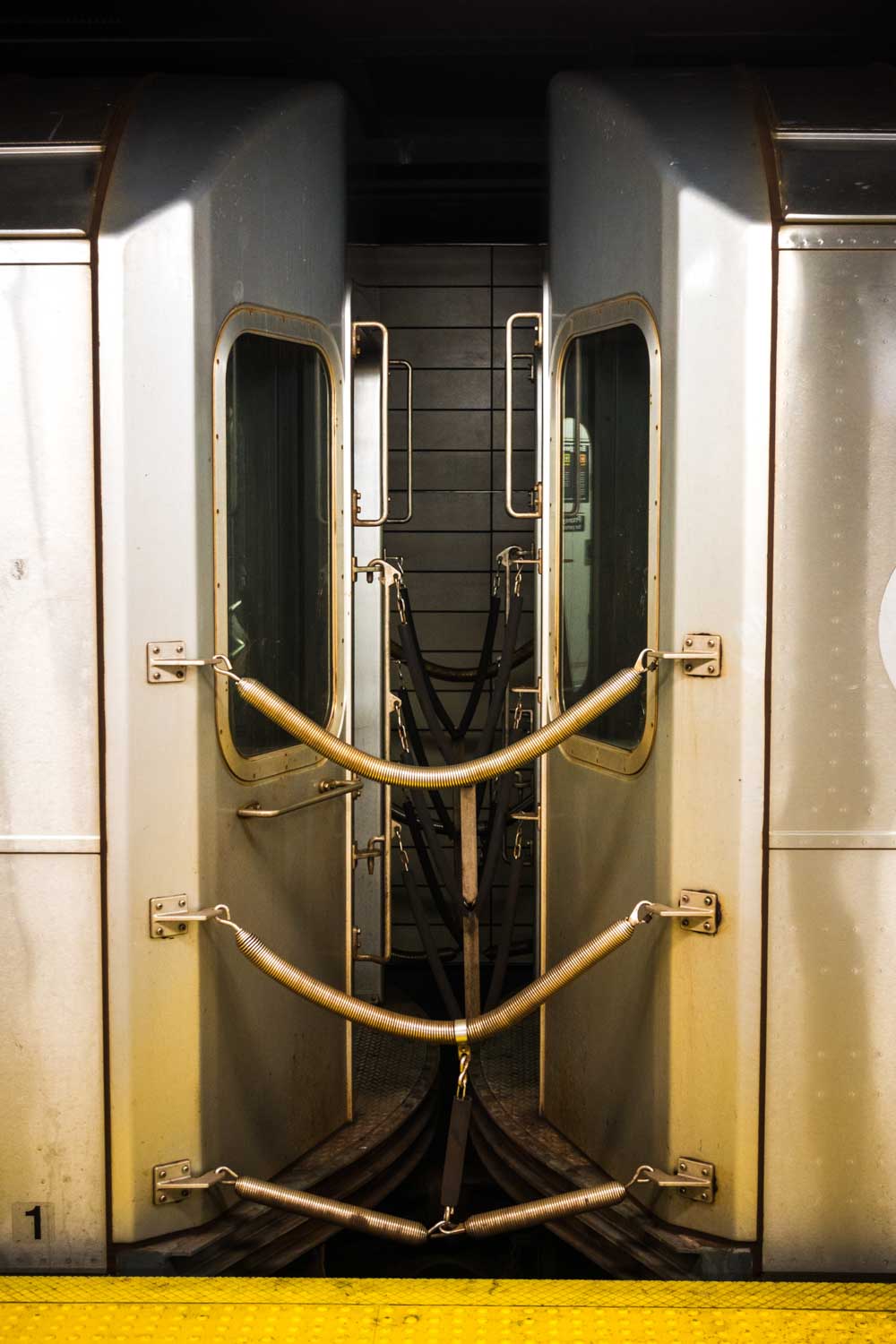 Close-up view of two connected train cars with metal rods and hoses visible at a subway station.