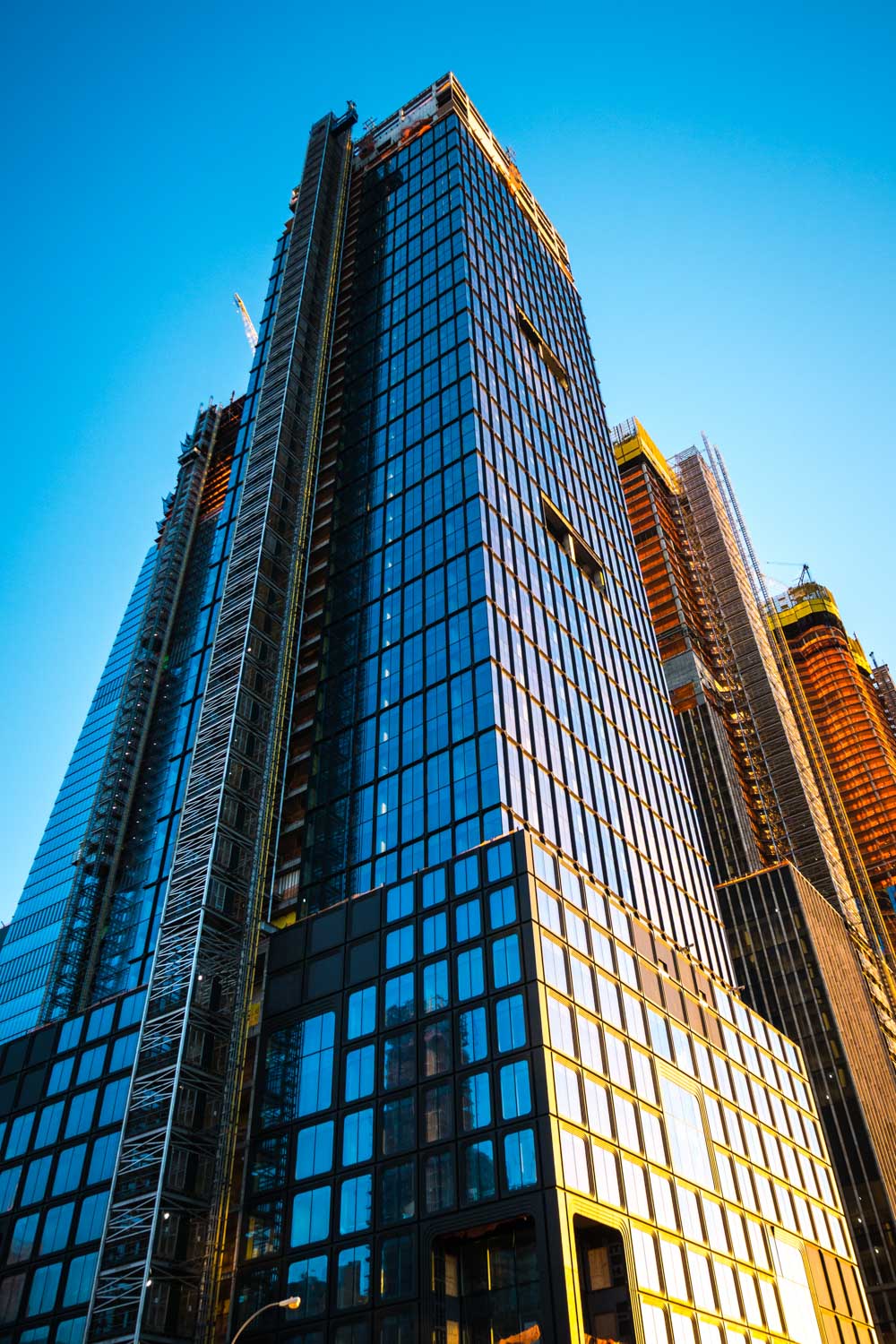 Modern skyscraper under construction against a clear blue sky, featuring glass facade and scaffolding.