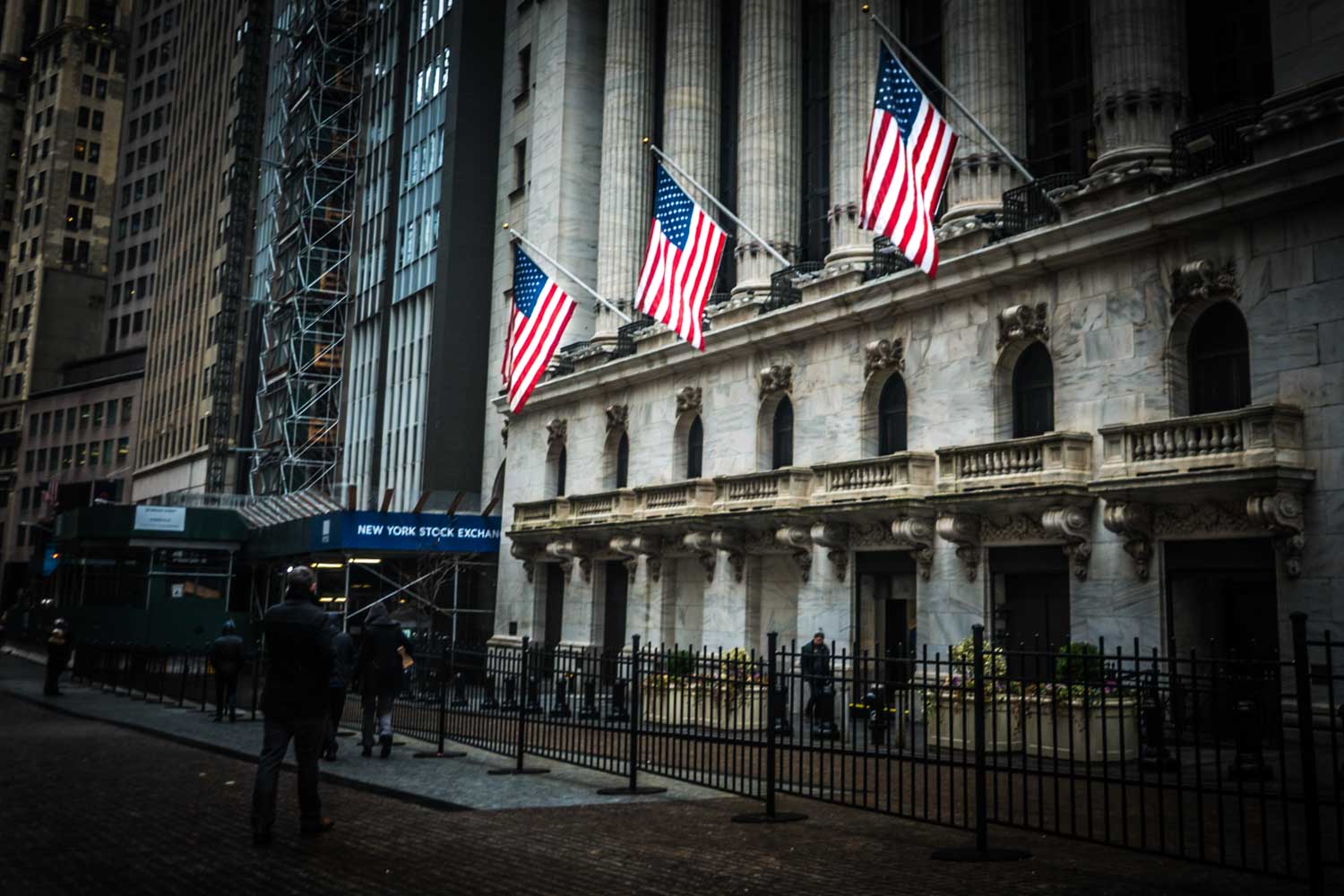 Facade of the New York Stock Exchange with American flags and people walking by.