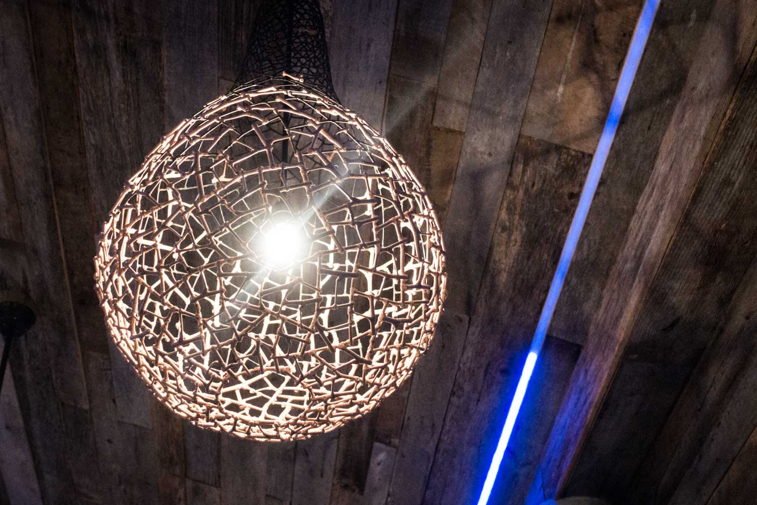 Hanging woven light fixture glowing on a wooden ceiling with blue neon strip accent.