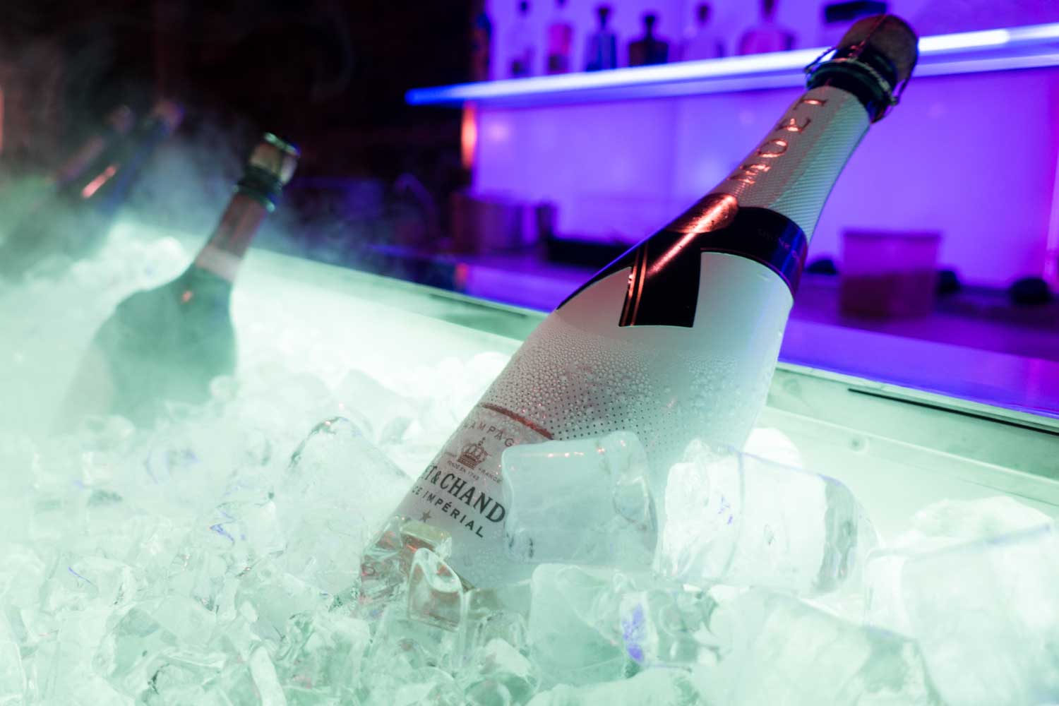 Chilled champagne bottles in ice bucket with purple-lit bar backdrop.