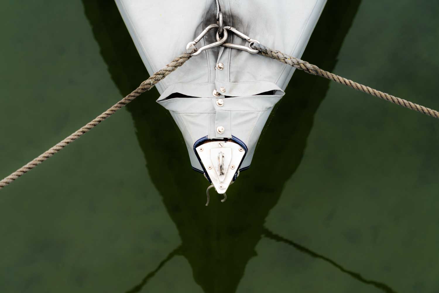 Boat bow covered with canvas, anchored with ropes over calm, green water.