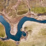 Aerial view of a meandering river through grassy terrain, creating natural curves and patterns in the landscape.