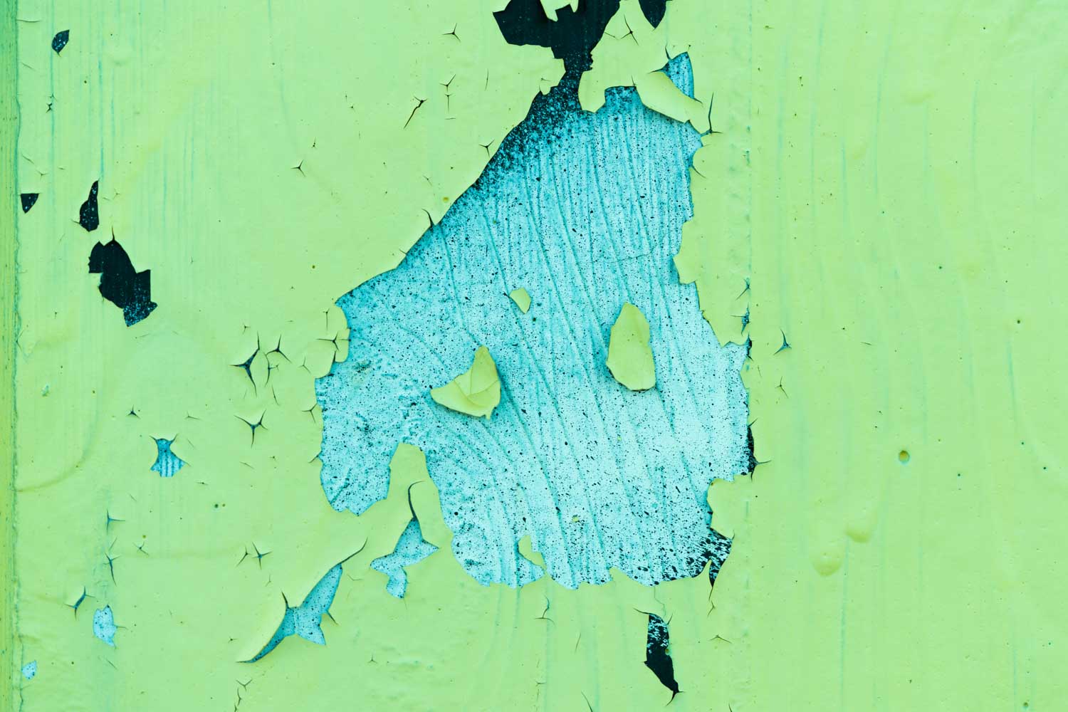 Close-up of peeling green paint revealing a textured blue layer underneath on a weathered wall surface.
