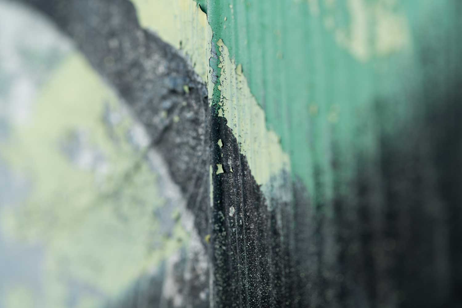Close-up of peeling green and black paint on a textured surface, showing layers and weathering.