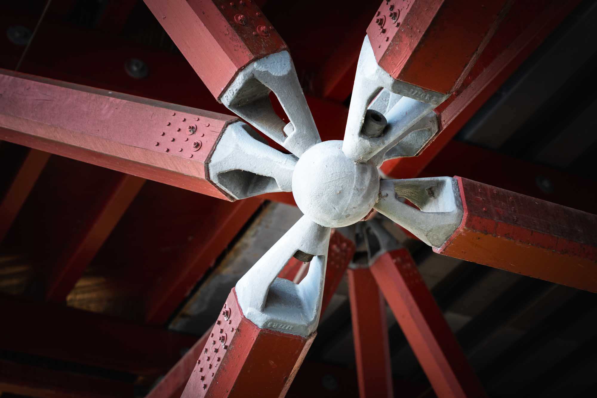 Red metal beams and central joint structure under a bridge, showcasing industrial engineering design.