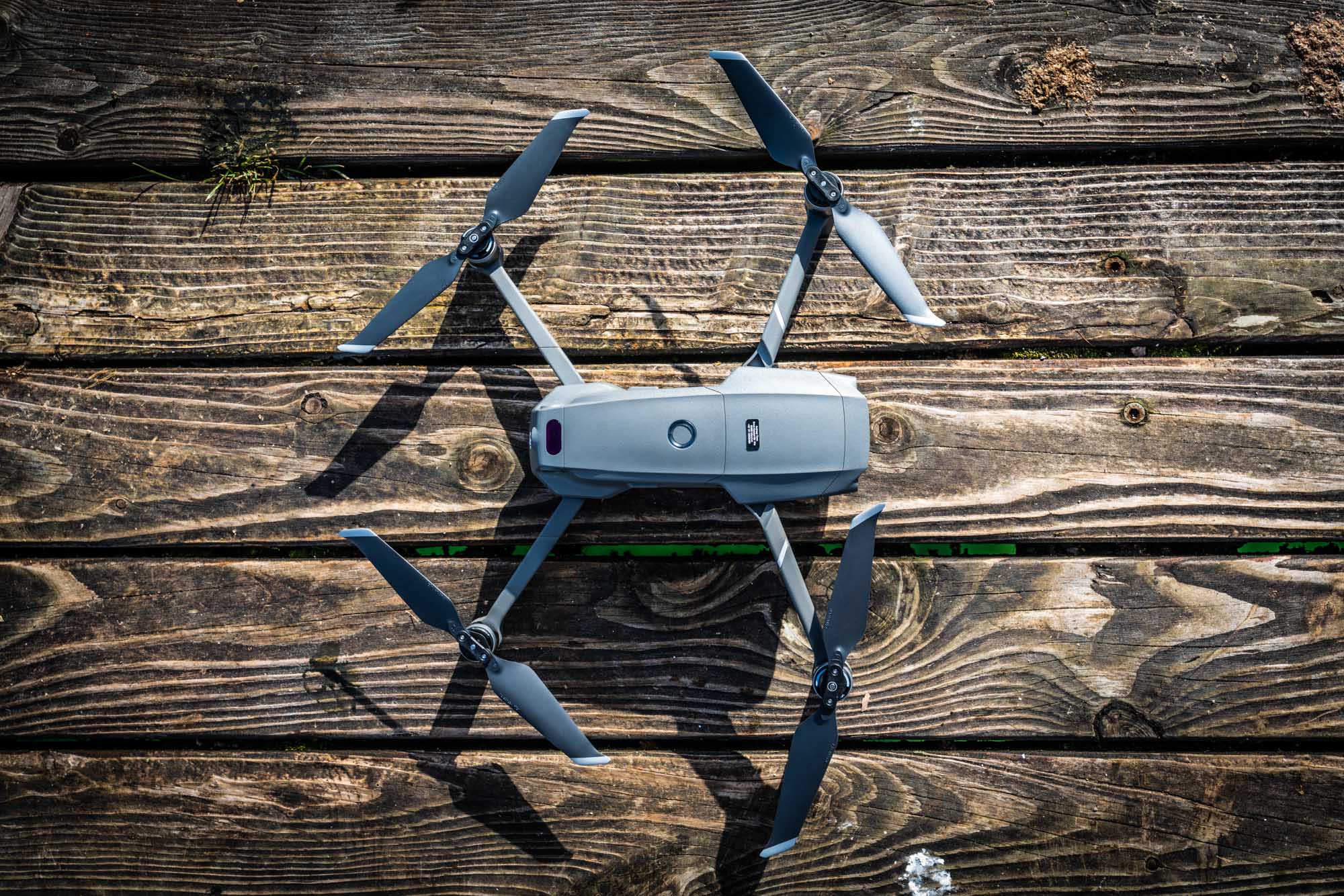 Quadcopter drone with four propellers on a wooden deck, viewed from above.