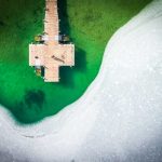 Aerial view of a wooden dock surrounded by green water and ice, creating a striking, nature-focused landscape scene.