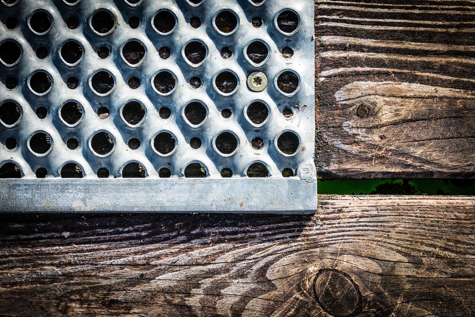 Metal perforated sheet with circular holes next to wooden planks, showing texture and contrast.