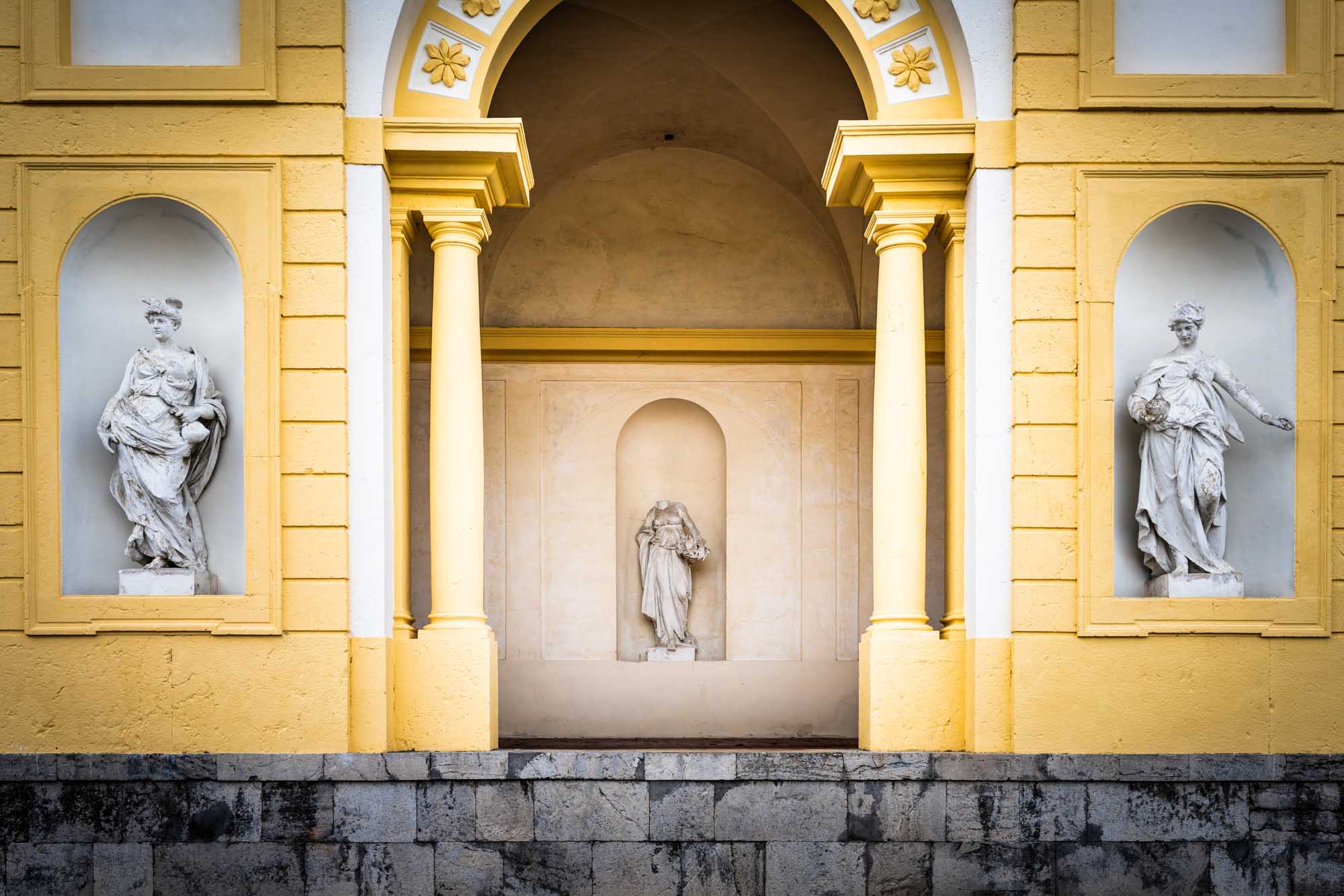 Yellow architecture with three classical statues in niches, framed by columns and decorative arches.