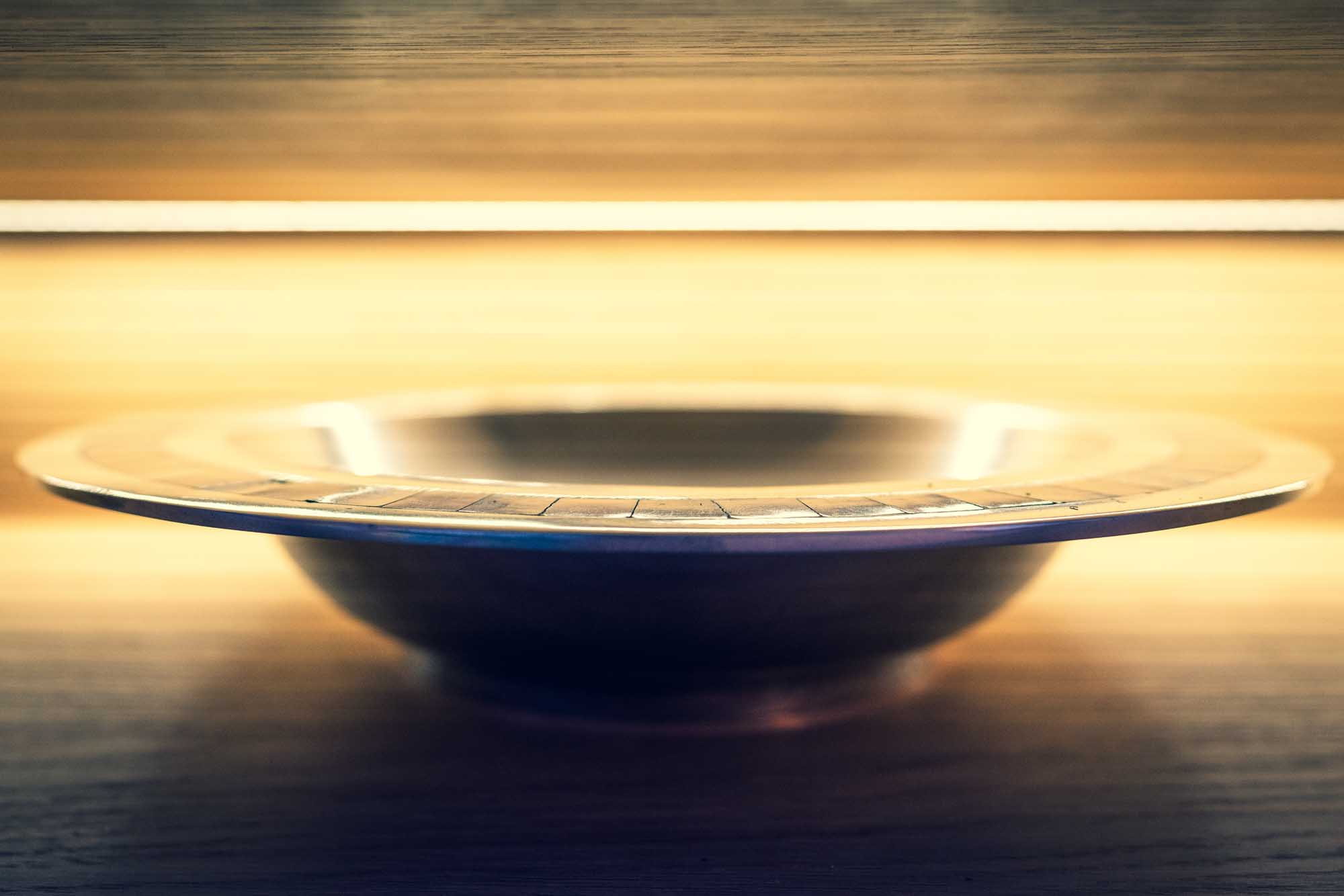 Illuminated silver bowl with engraved details on a wooden surface, under warm ambient lighting.