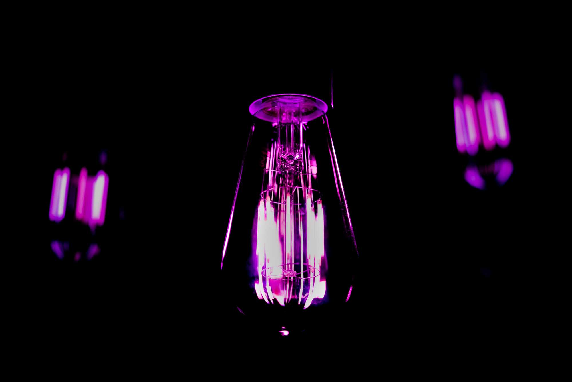 Glowing purple light bulb against a dark background, illuminating with vibrant neon hues.