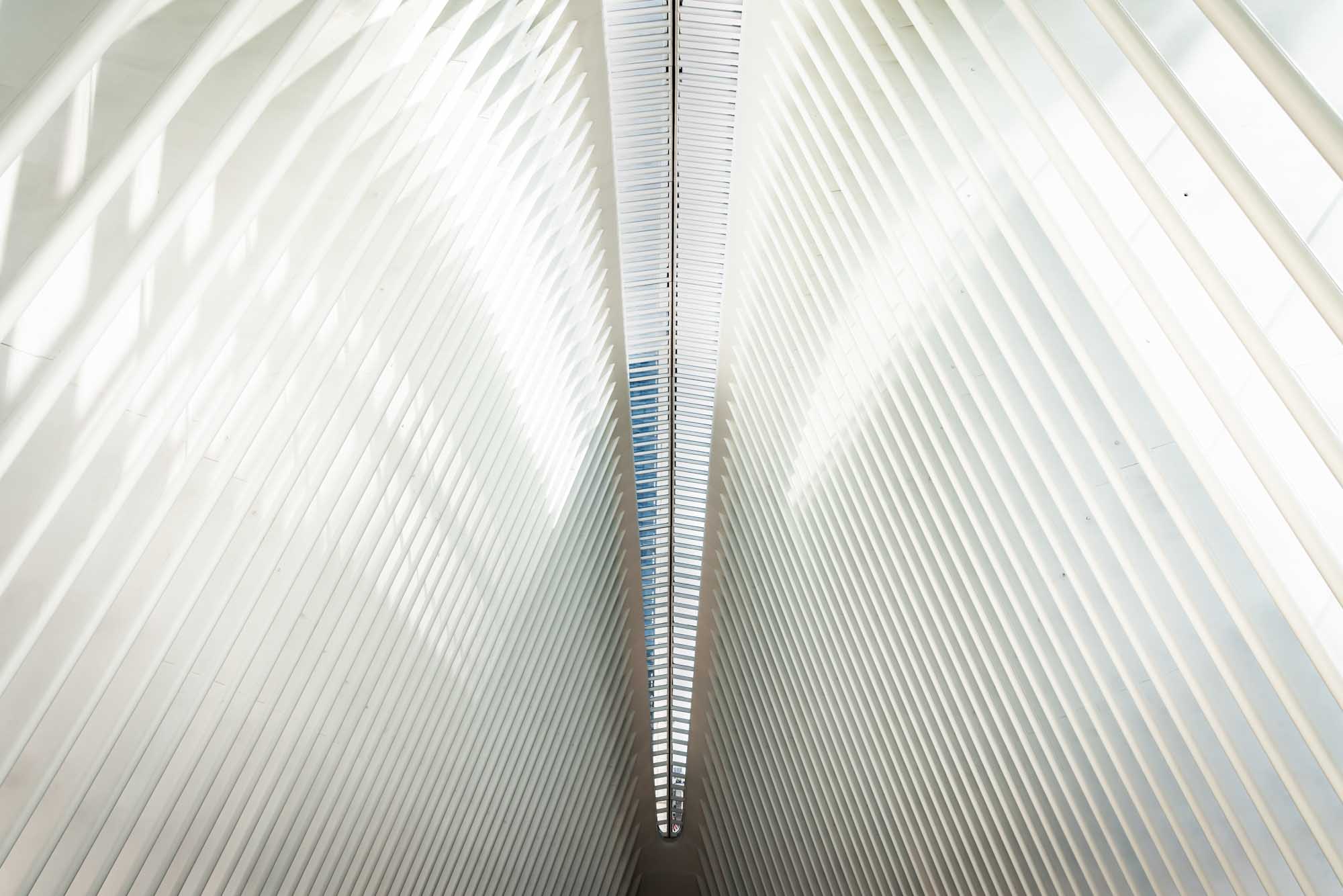 Futuristic architectural ceiling with converging white beams and skylight, creating a sleek, symmetrical design.