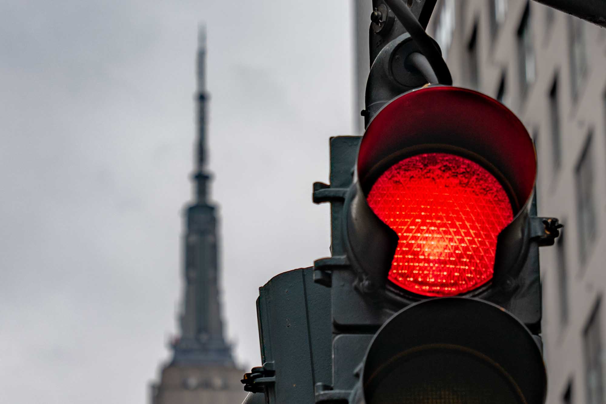 Red traffic light with a blurred skyscraper in the background, overcast sky.