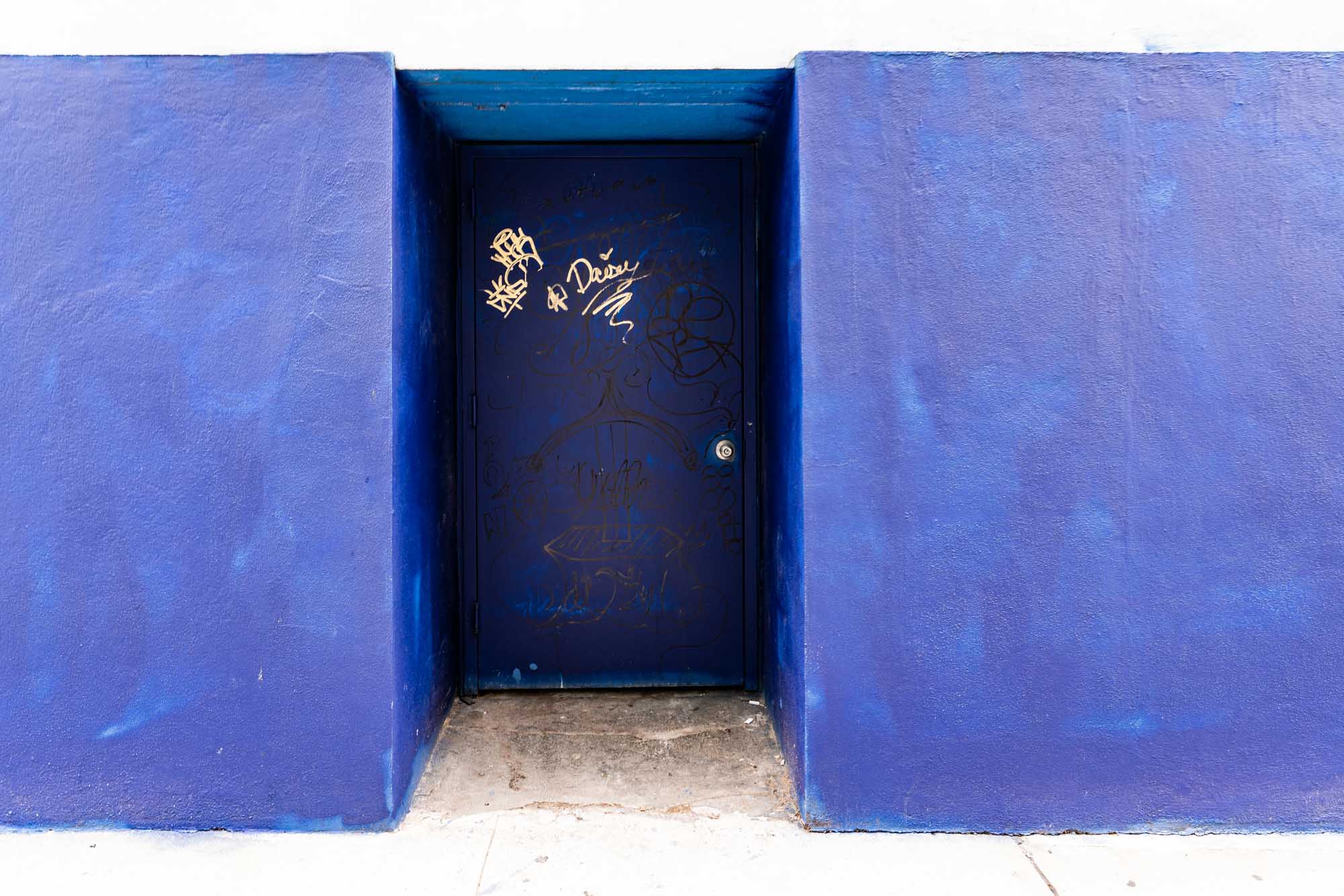 Blue wall with a dark door featuring artistic graffiti and a blue frame.