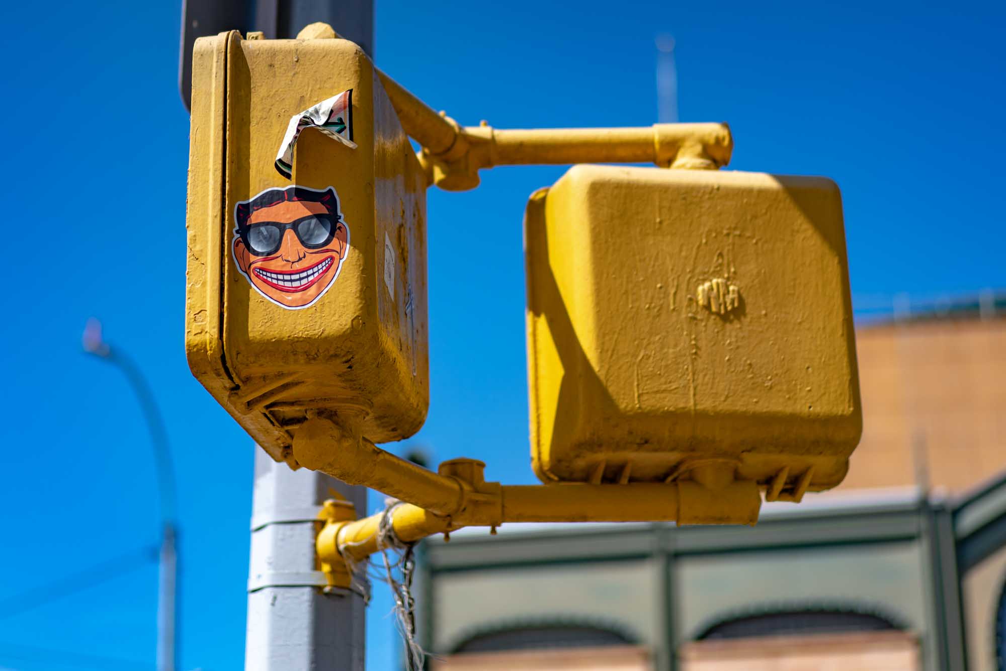 Yellow traffic signal with smiling face sticker and blue sky background.