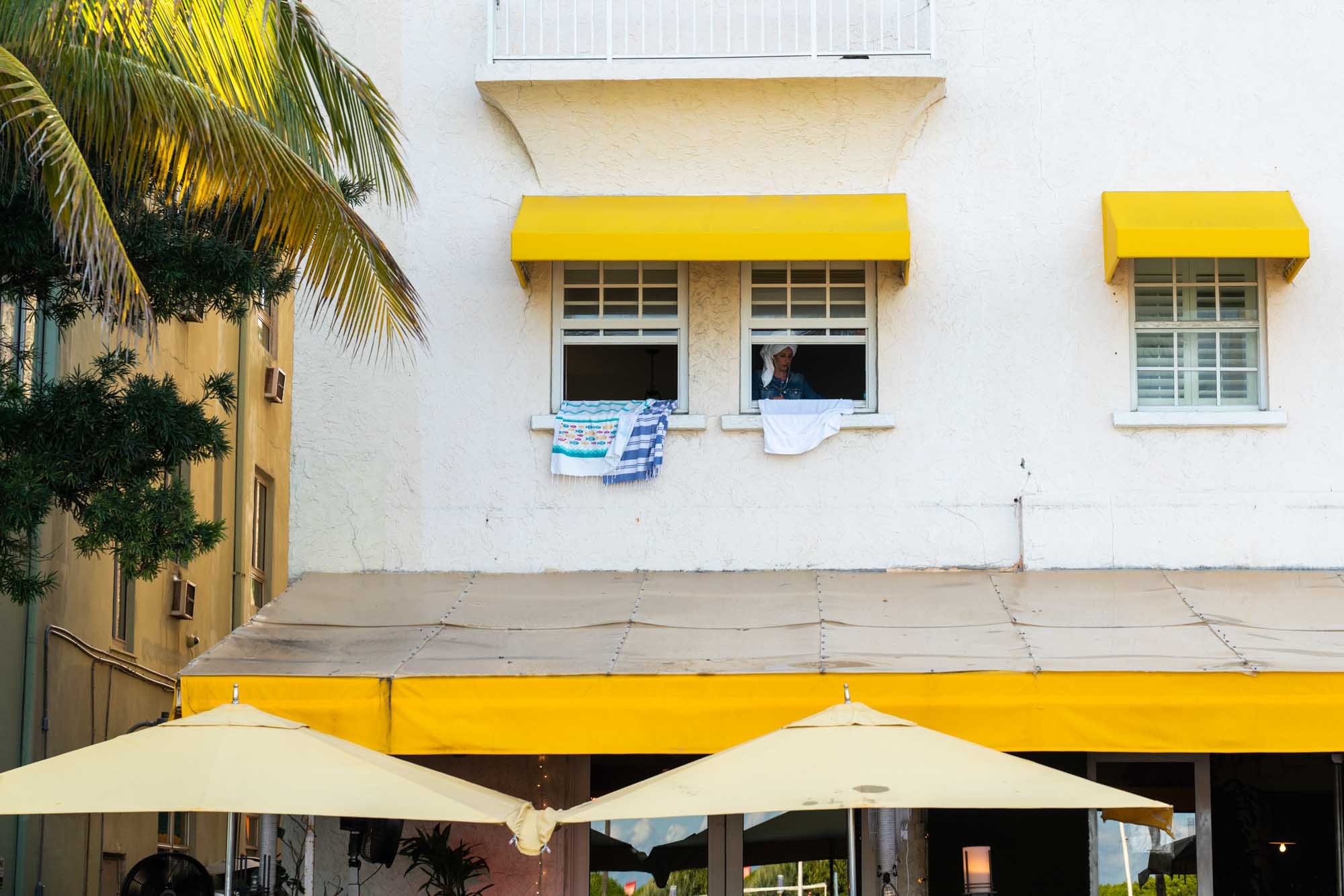 Yellow awnings and umbrellas on a white building, person looking out an open window with clothes hanging.