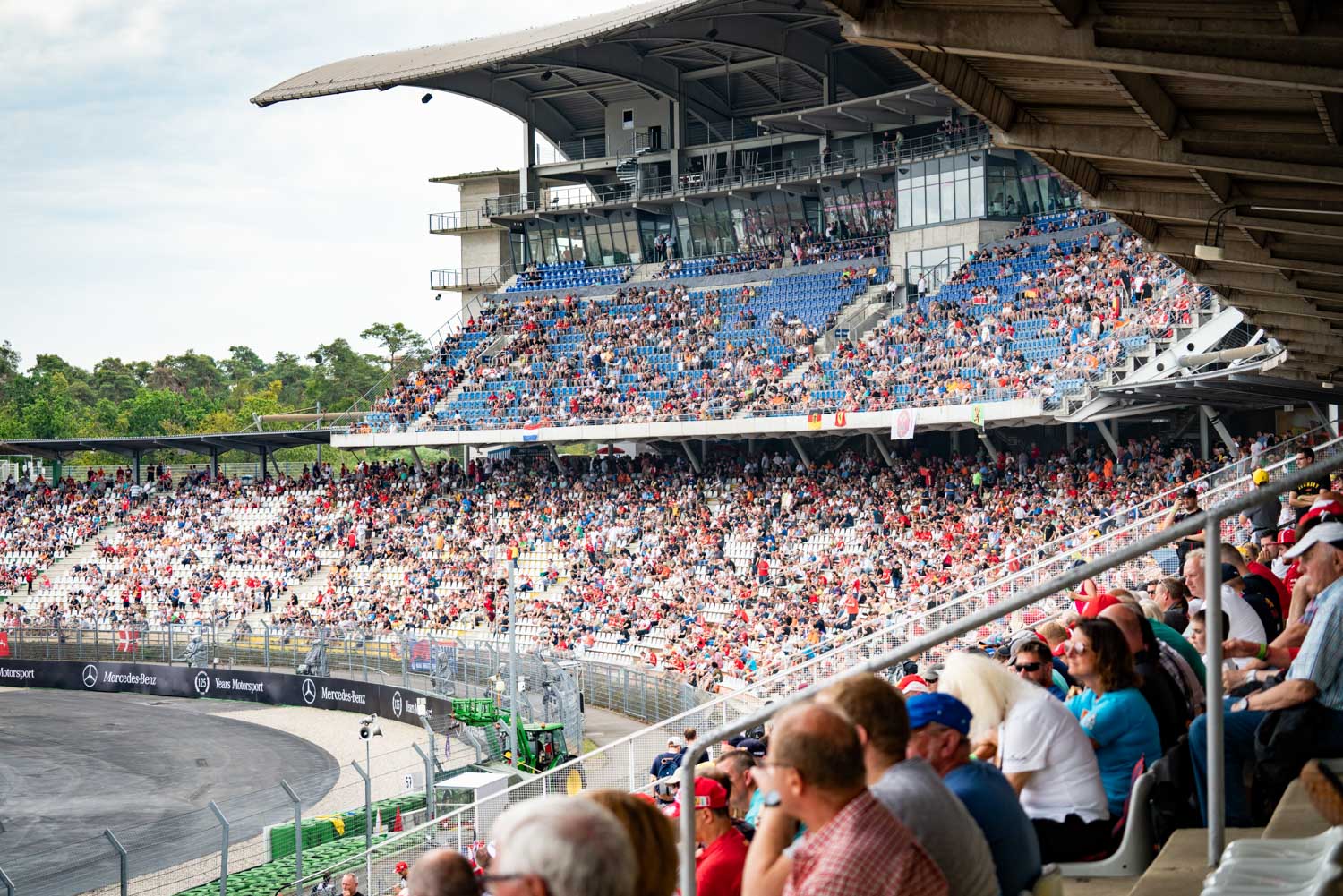 Crowded outdoor stadium with spectators, blue seats, and race track.