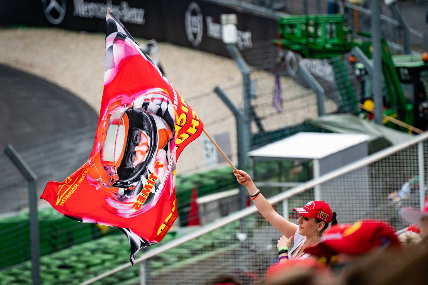 Spectator in red cap waves vibrant flag with racing helmet at motorsport event.