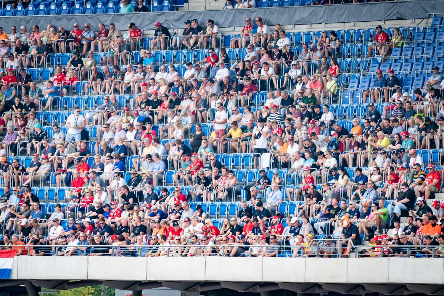 Crowd of spectators in blue stadium seats at an outdoor sports event, many wearing red shirts and caps.