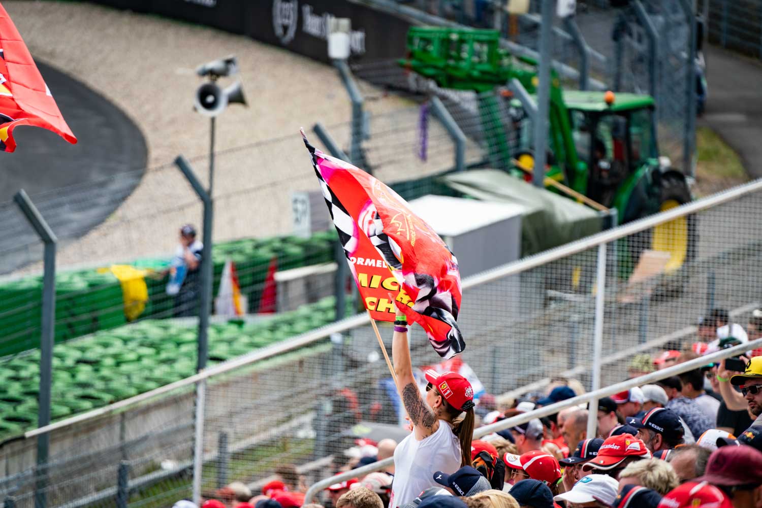 Spectator waving a red racing flag in crowded grandstand at a motorsport event.
