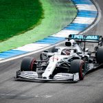 Formula 1 car racing on track with vibrant green and blue curbs, showcasing speed and precision driving.