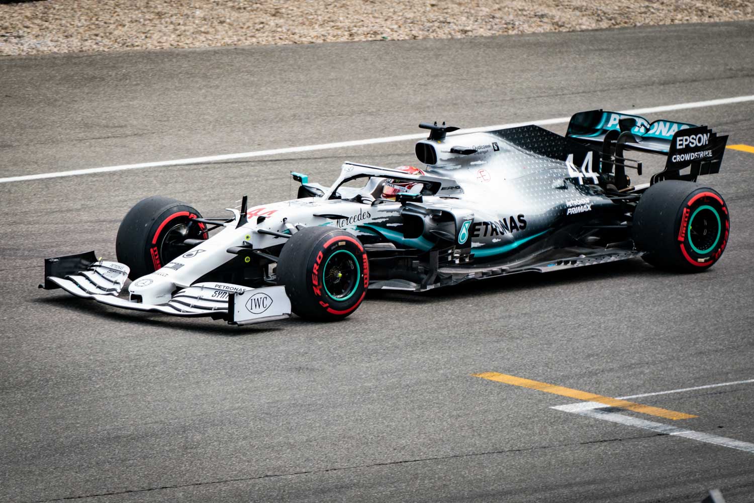 Silver Mercedes F1 car on racetrack, displaying sponsor logos and red Pirelli tires, captured during a race.