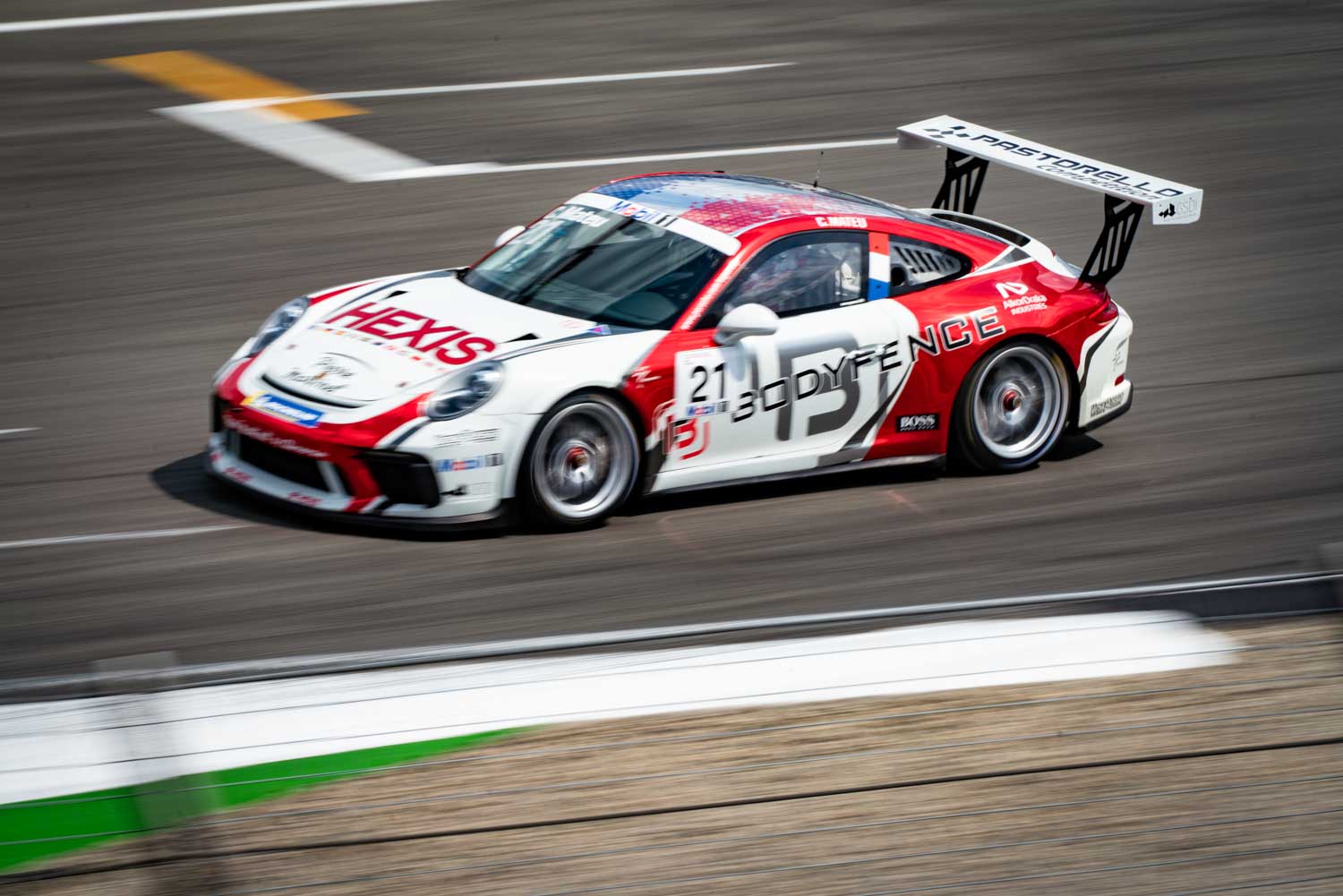 Race car with red and white HEXIS branding on track speeding past, showcasing dynamic motion and sleek design.