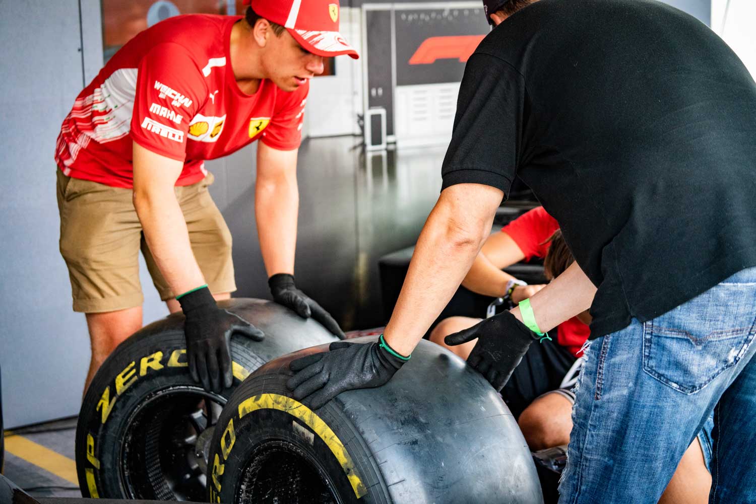 Mechanics wearing gloves handle race car tires in a pit garage for a motorsport event.