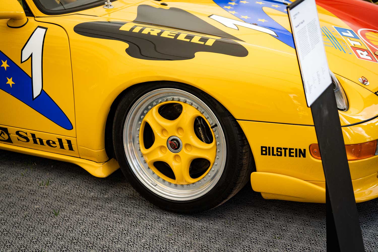 Close-up of a yellow race car showcasing a branded Pirelli tire, Bilstein logo, and number 1 decal on the body.