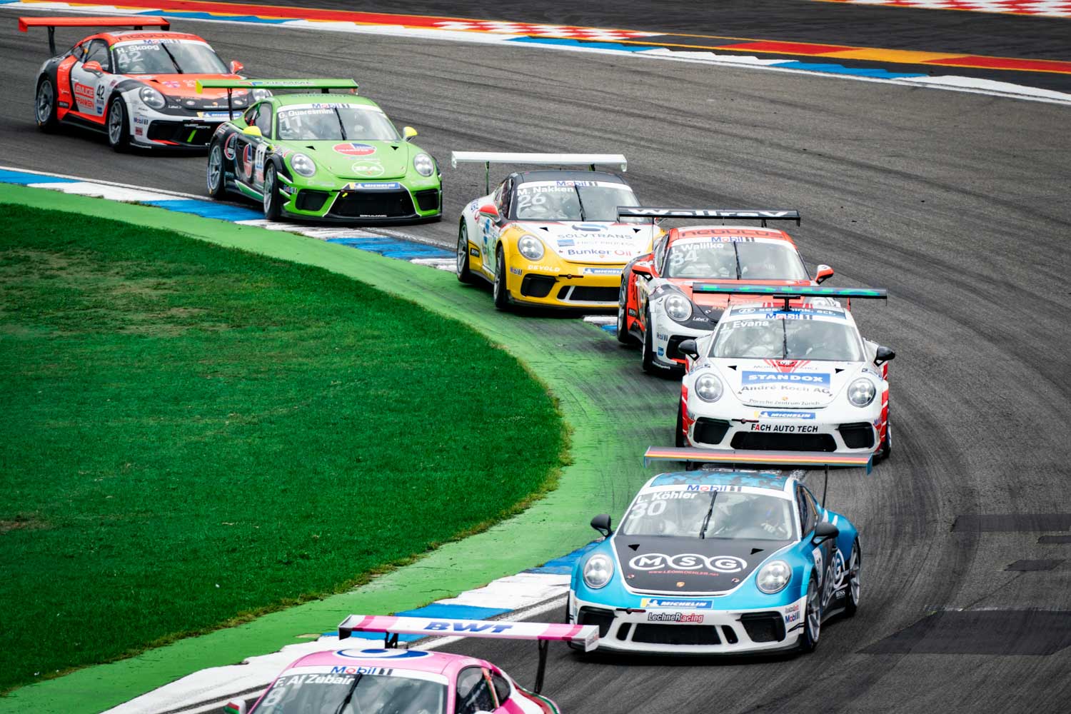 Race cars on a track curve during a competitive motorsport event, featuring colorful vehicles in action.