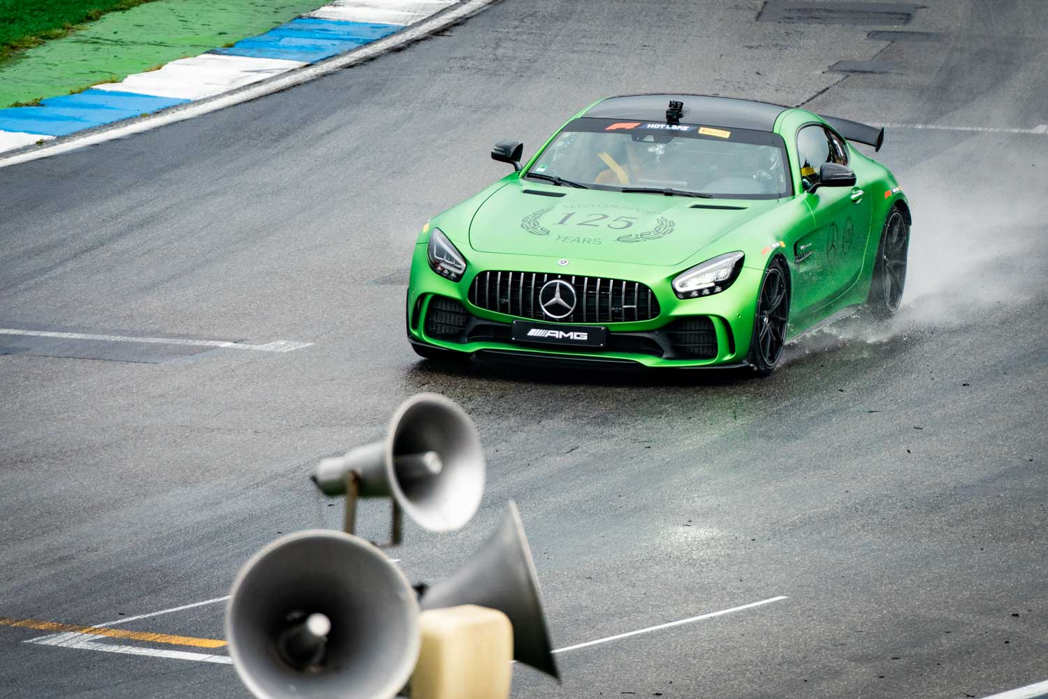 Green sports car drifting on wet racetrack, spraying water, with loudspeakers in the foreground.