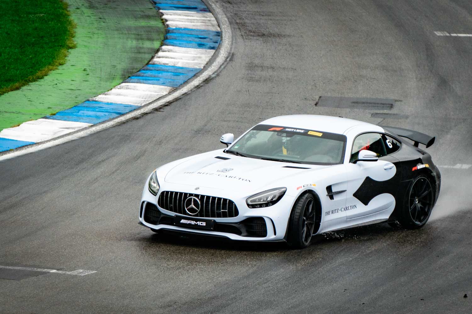 White Mercedes-AMG sports car drifting on wet race track, showcasing dynamic handling and performance.