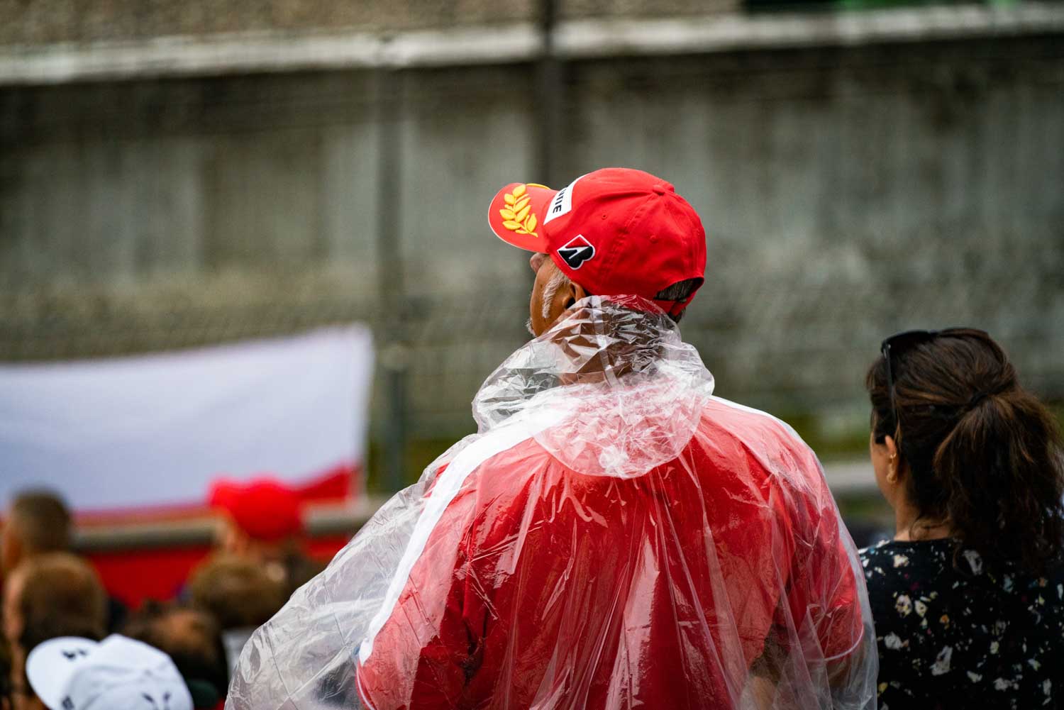 Man in red cap and rain poncho at outdoor event, crowd in background.