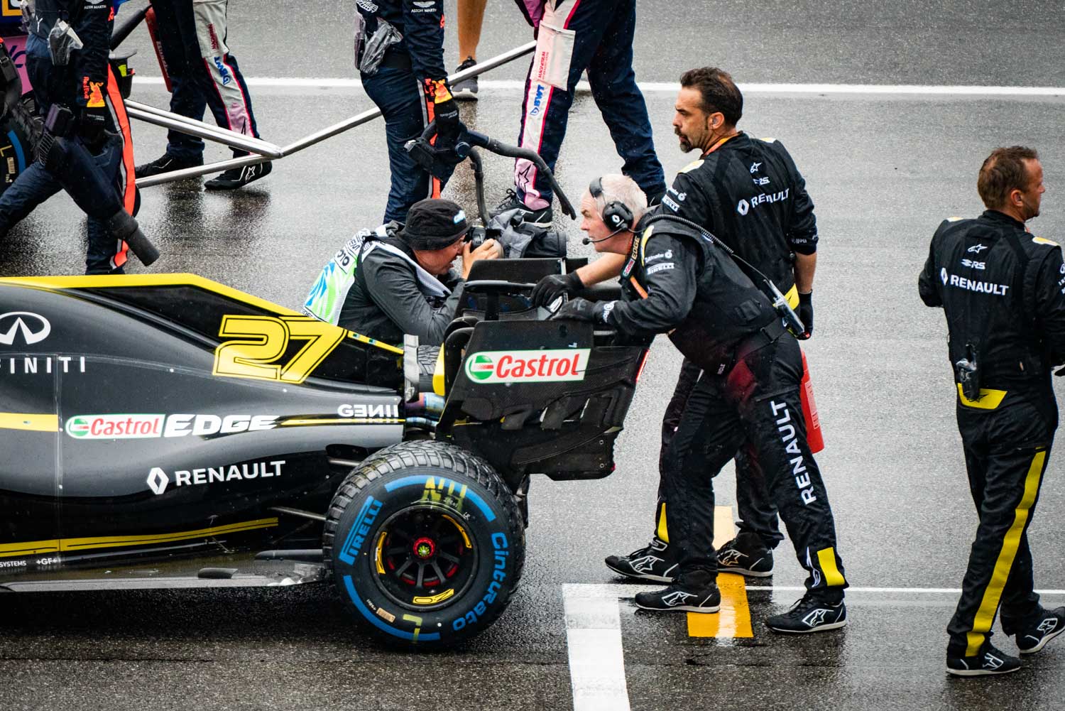 Racing crew prepares Renault F1 car in wet conditions on track, with team members adjusting parts and checking equipment.