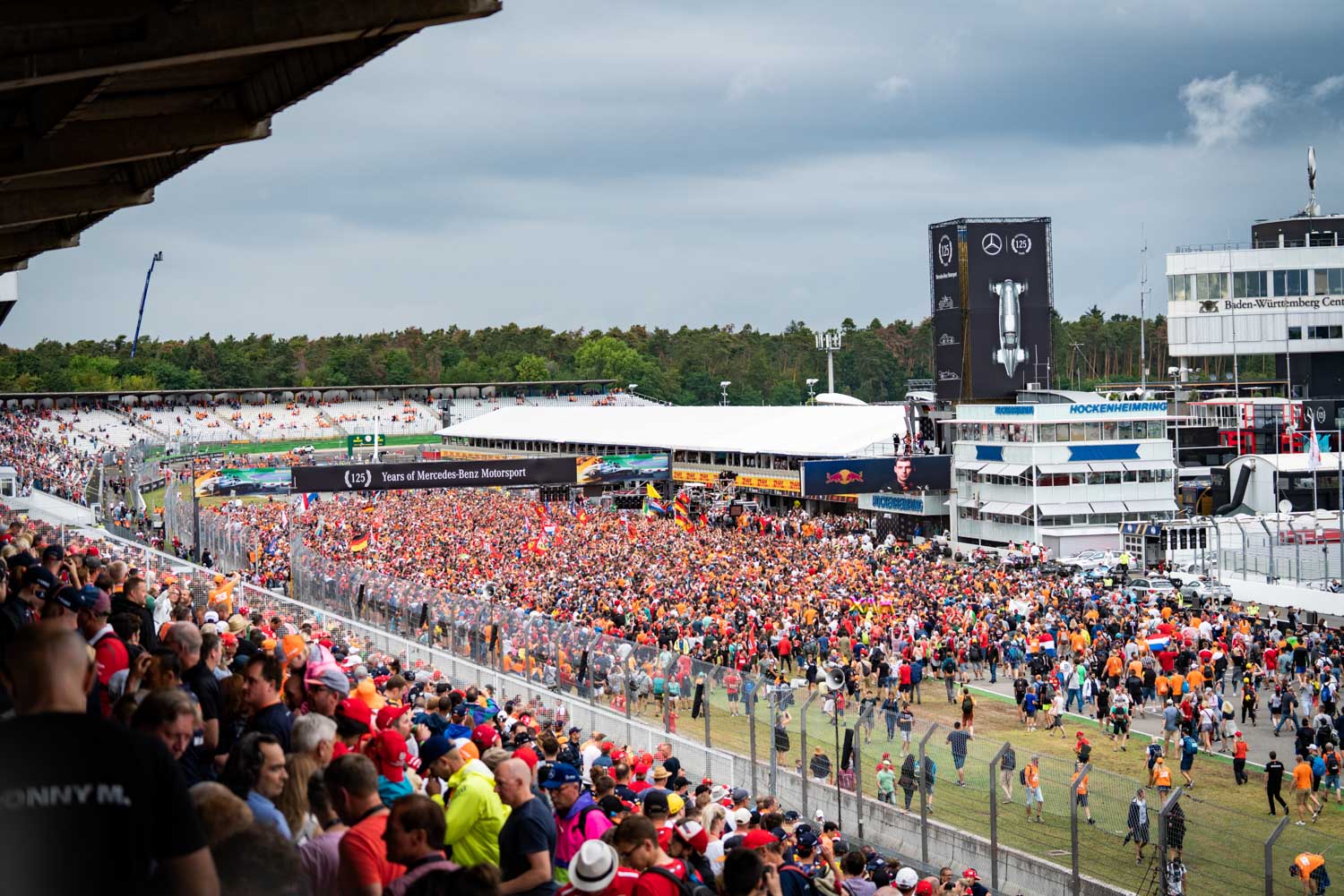Large crowd at Hockenheimring race track event with Mercedes-Benz banners, celebrating motorsport anniversary.