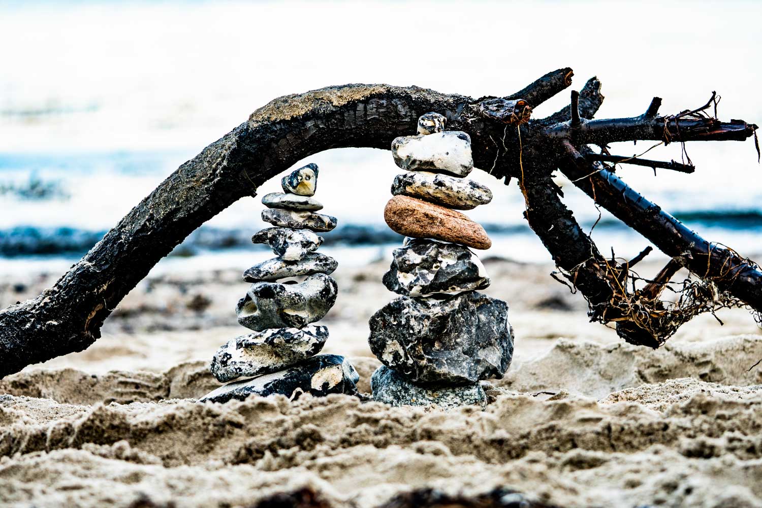 Stacked stones beneath a curved tree branch on a sandy beach background.