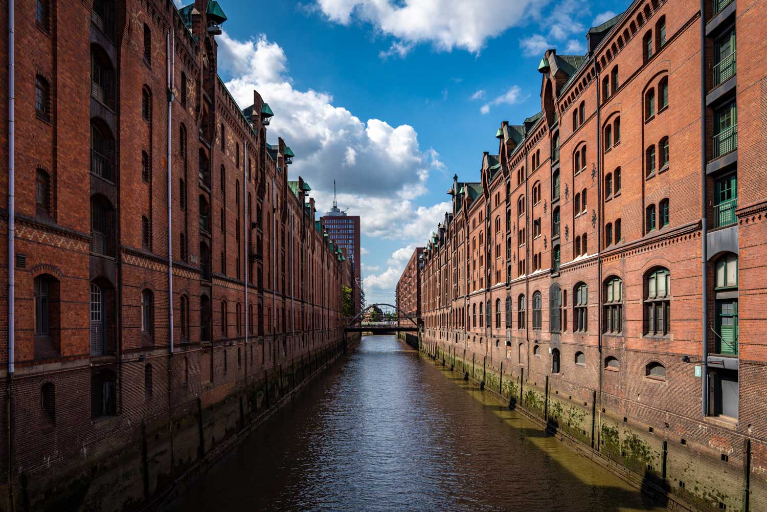 Brick canal warehouses under blue sky with clouds in Hamburg's Speicherstadt district.
