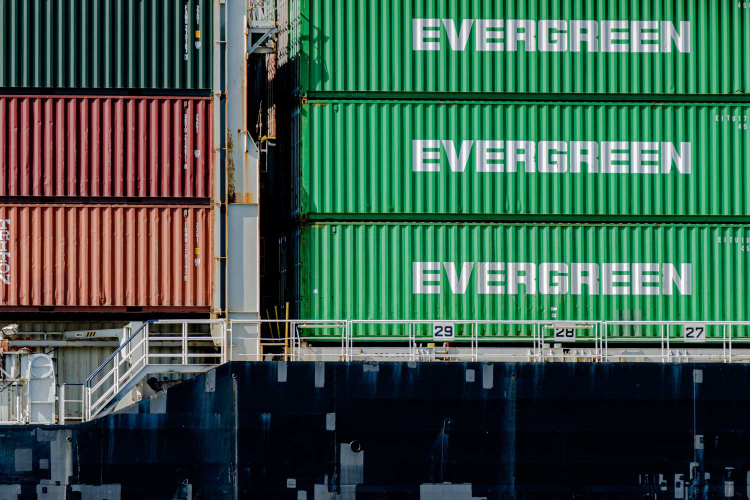 Green and red shipping containers stacked on a cargo ship, with EVERGREEN logos prominently displayed.